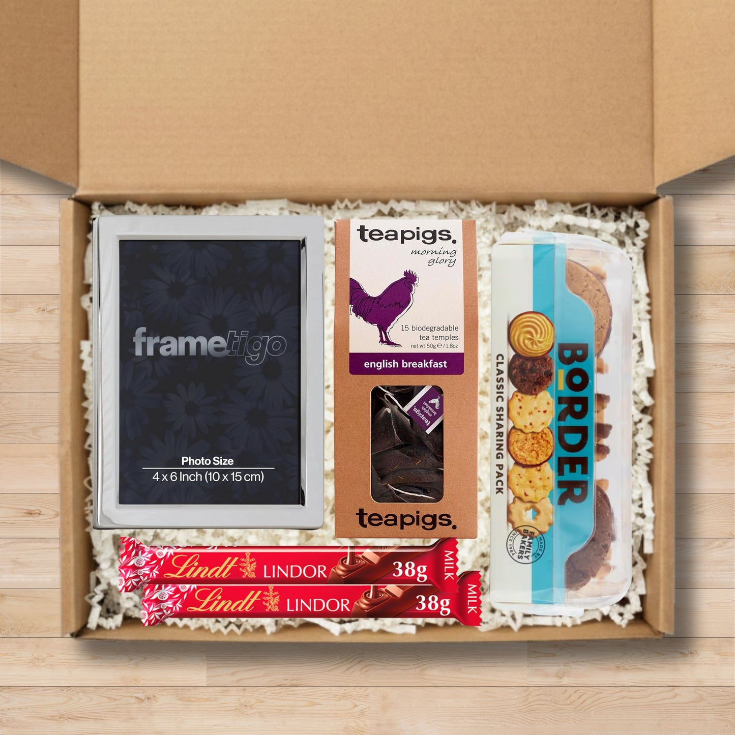 Gift box containing a photo frame, teapigs tea temples, border classic sharing pack of biscuits, and Lindt chocolate bars.