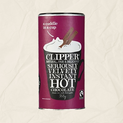 A tub of Clipper Instant Hot Chocolate, featuring a deep magenta label with a black mug illustration and white text, set against a textured off-white background.
