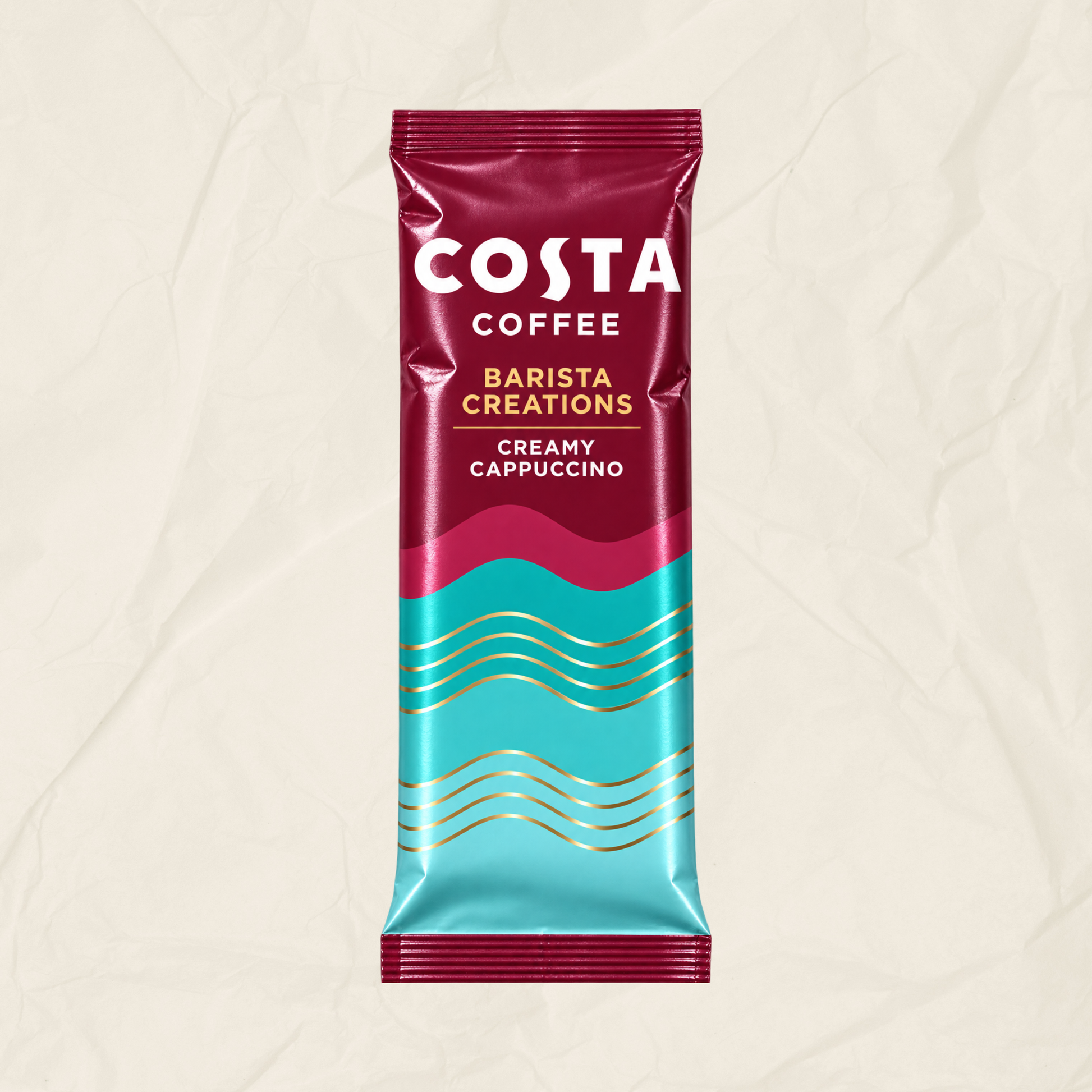 A single Costa Coffee Barista Creations Creamy Cappuccino sachet standing upright on a textured beige background. The packaging features a deep magenta top half with white branding, a bright turquoise bottom half with gold wavy lines, and a magenta-to-turquoise gradient center.