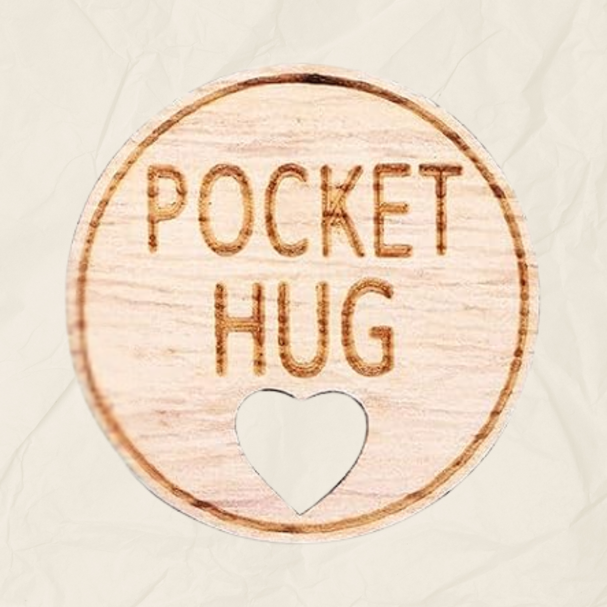 A round wooden token with the text "Pocket Hug" laser etched into it and a heart shaped hole, designed to be kept in the recipients pocket.