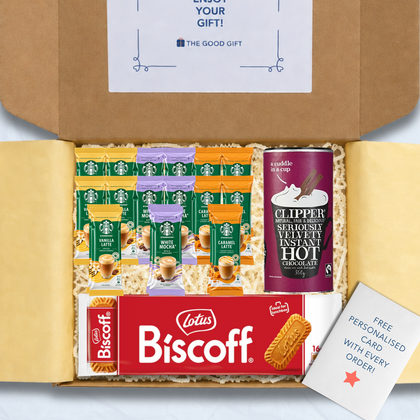 A curated gift box filled with packaged snacks and biscuits, including Starbucks coffee sachets, a pack of Lotus Biscuit, a Clipper 350g tub of hot chocolate, and a free personalised card, shown from above inside an open brown cardboard box.