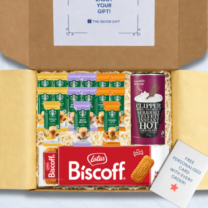 A curated gift box filled with packaged snacks and biscuits, including Starbucks coffee sachets, a pack of Lotus Biscuit, a Clipper 350g tub of hot chocolate, and a free personalised card, shown from above inside an open brown cardboard box.