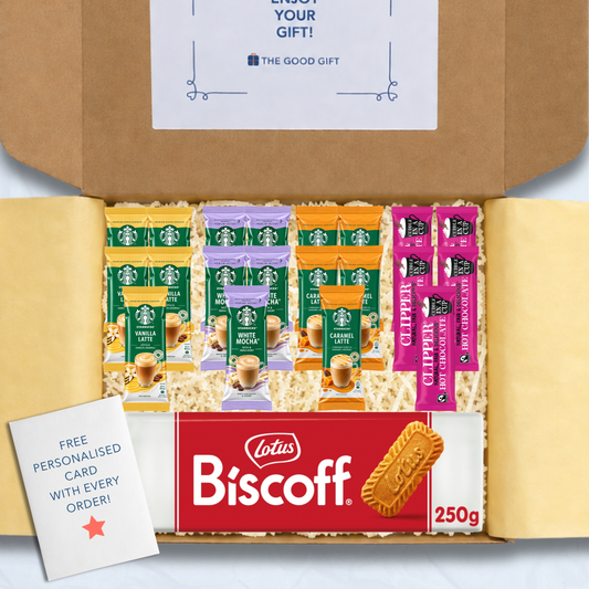 A curated gift box filled with packaged snacks and biscuits, including Starbucks coffee sachets, a pack of Lotus Biscuit, a Clipper 350g tub of hot chocolate, and a free personalised card, shown from above inside an open brown cardboard box.