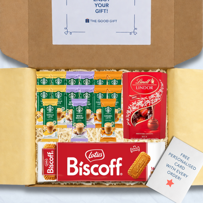 A curated gift box filled with packaged snacks and biscuits, including Starbucks coffee sachets, a pack of Lotus Biscuit, a Lindt Lindor 200g box of milk chocolate truffles, and a free personalised card, shown from above inside an open brown cardboard box.