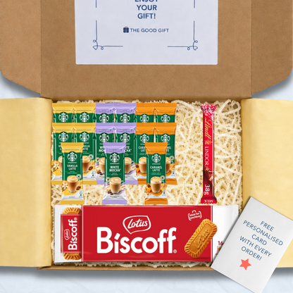 A curated gift box filled with packaged snacks and biscuits, including Starbucks coffee sachets, a pack of Lotus Biscuit, a Lindt Lindor 38g milk chocolate bar, and a free personalised card, shown from above inside an open brown cardboard box.