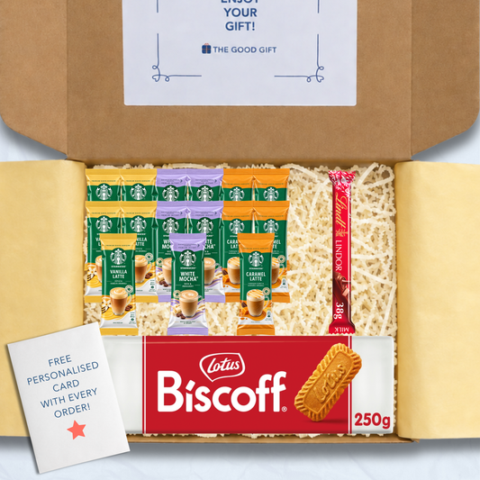 A curated gift box filled with packaged snacks and biscuits, including Starbucks coffee sachets, a pack of Lotus Biscuit, a Lindt Lindor 38g milk chocolate bar, and a free personalised card, shown from above inside an open brown cardboard box.