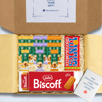 A curated gift box filled with packaged snacks and biscuits, including Starbucks coffee sachets, a pack of Lotus Biscuit, a Tony's Chocolonely milk chocolate bar, and a free personalised card, shown from above inside an open brown cardboard box.