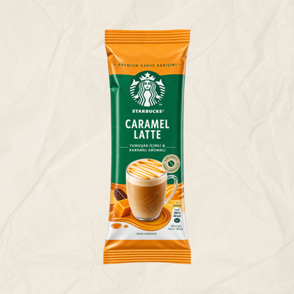 A single packet of Starbucks Caramel Latte instant coffee on a textured beige background. The packaging features a green and orange design with a photo of a caramel latte in a glass mug.