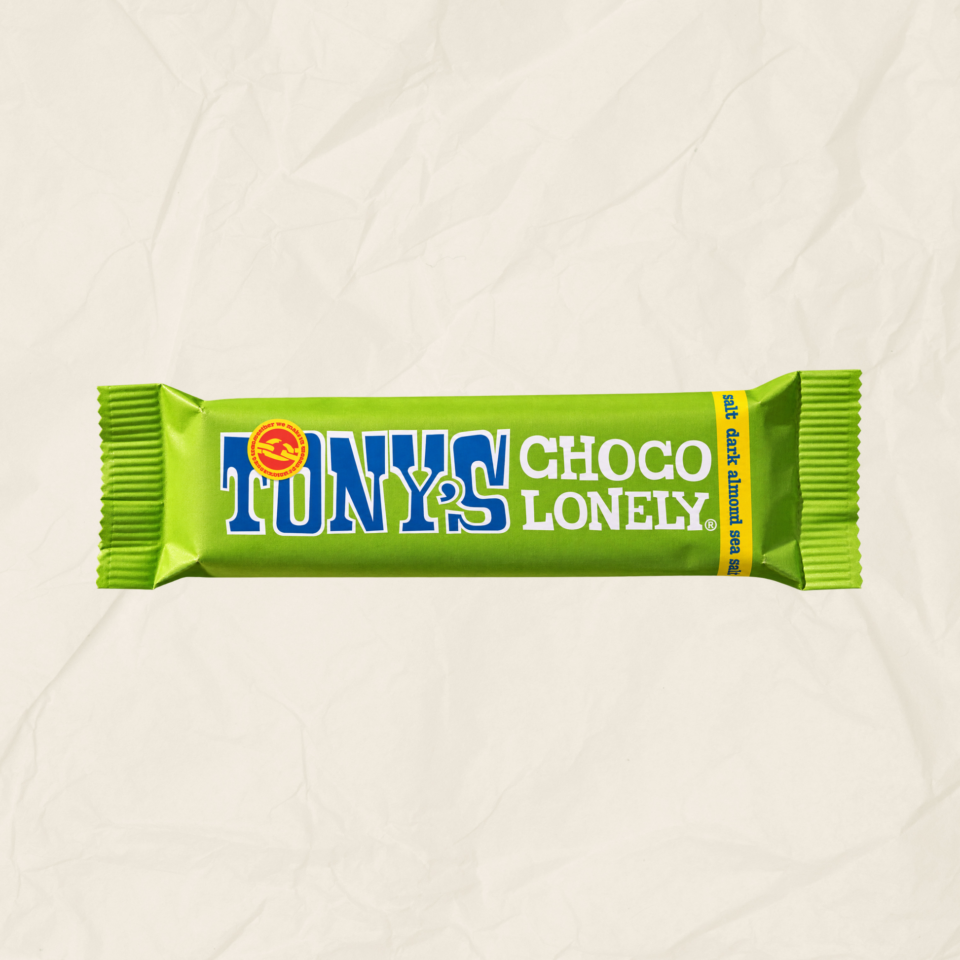 A single Tony's Choco Lonely chocolate bar wrapper in bright lime green, with blue and white lettering, centered on a light beige crumpled paper background.