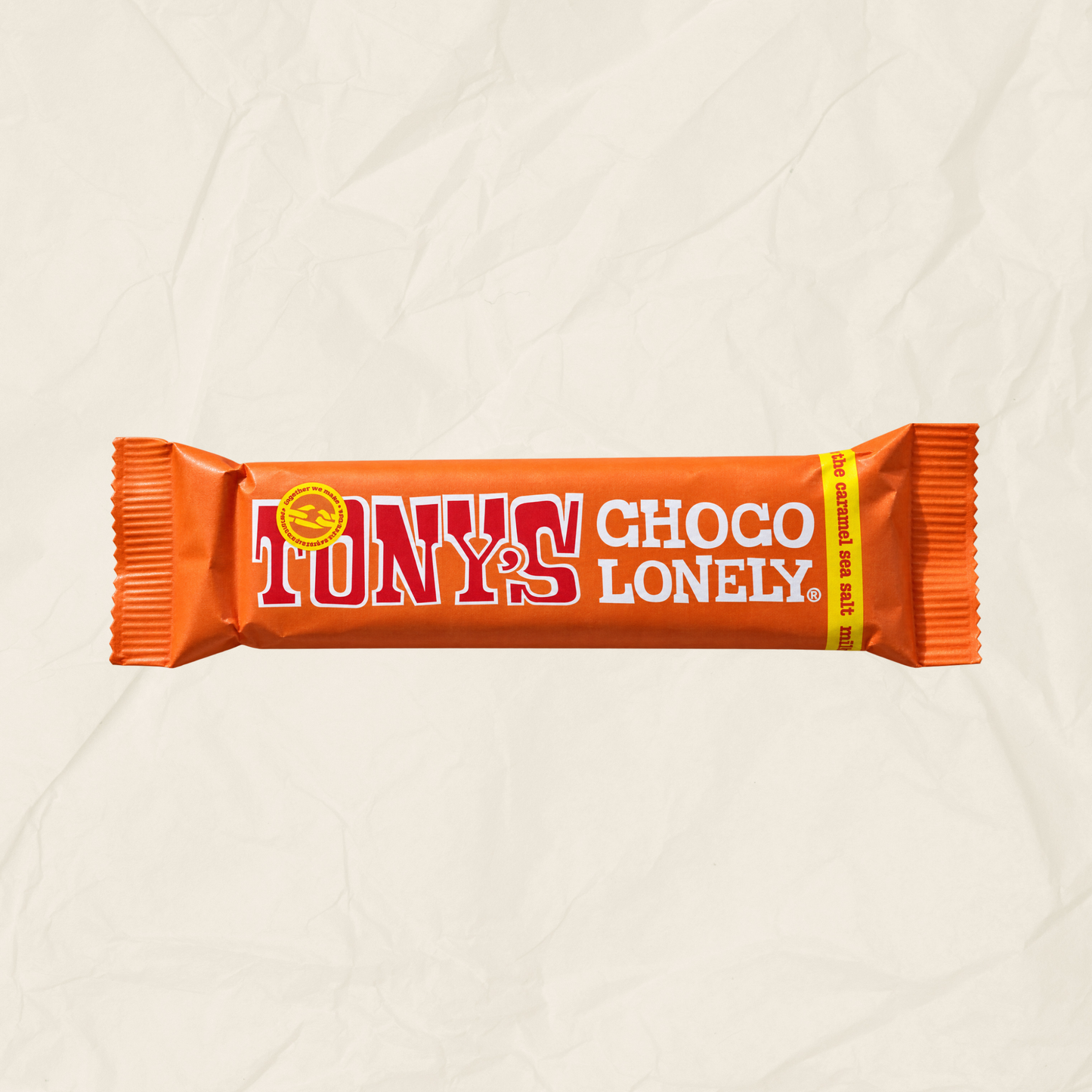 A single Tony's Choco Lonely chocolate bar in its signature orange wrapper, displayed horizontally against a textured, crumpled off-white paper background.