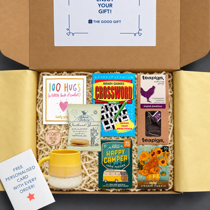 Gift box containing Teapigs english breakfast tea, a 100 Hugs book, shortbread biscuits, a Happy Camper game, a masterworks jigsaw puzzle, a crossword book, a yellow mug, and a pocket hug