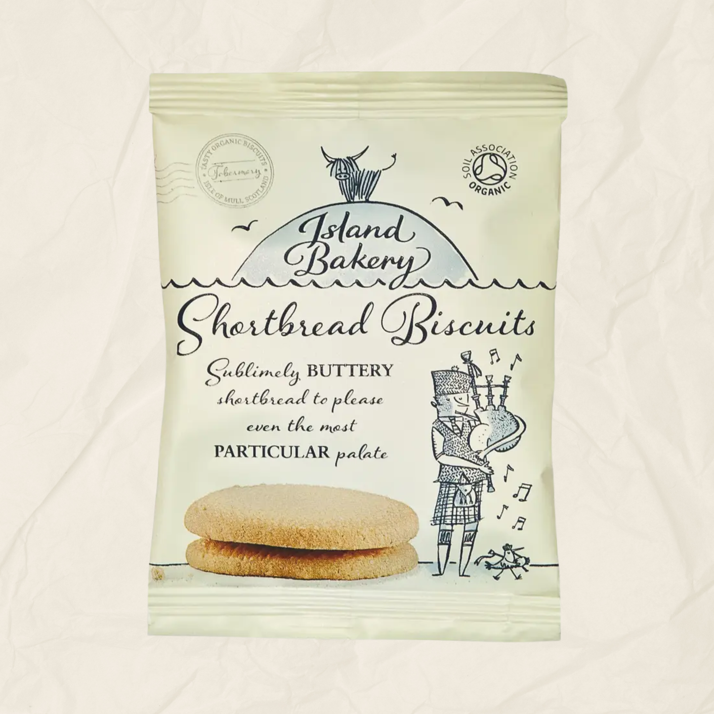 A package of Island Bakery Shortbread Biscuits on a textured off-white background. The packaging is cream-colored with black text and illustrations of a cow, birds, and a kilted figure playing bagpipes, with two biscuits pictured at the bottom.