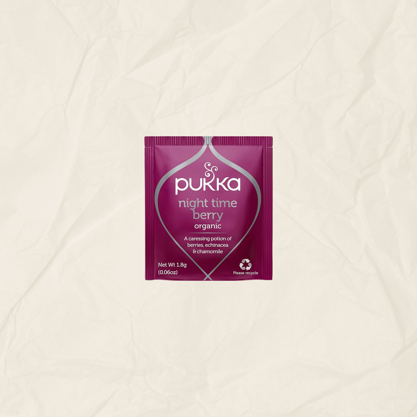 A single packet of Pukka Night Time Berry Organic herbal tea centered on a textured, crumpled off-white paper background.