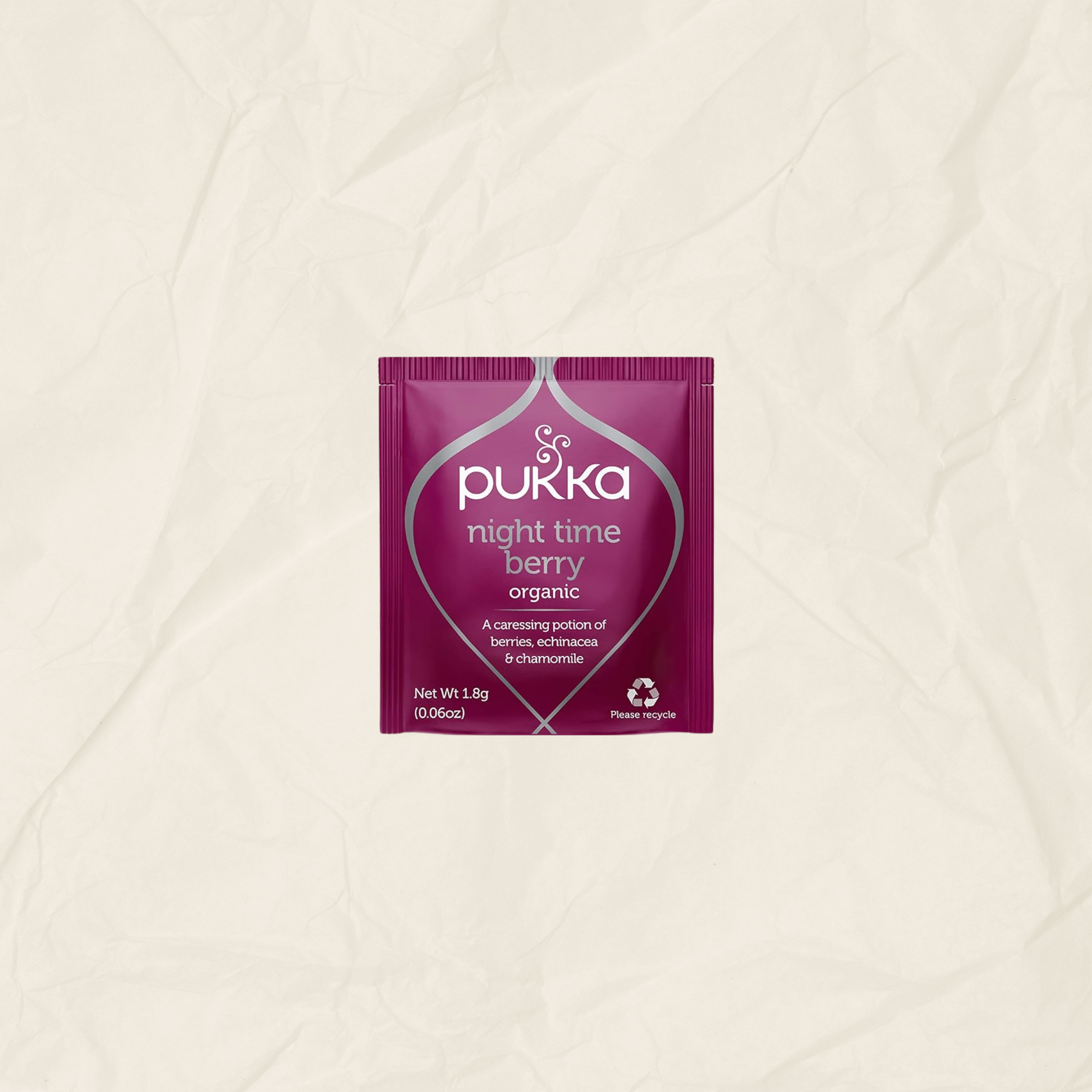 A single packet of Pukka Night Time Berry Organic herbal tea centered on a textured, crumpled off-white paper background.