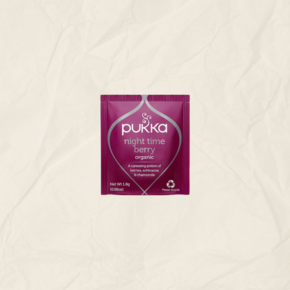 A single packet of Pukka Night Time Berry Organic herbal tea centered on a textured, crumpled off-white paper background.