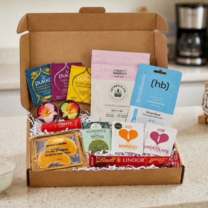 A gift box containing pukka tea, bath salts, tea lights, under-eye masks, Lindt Lindor chocolate, matcha cookies, and I Love Snacks Mango and Chocolate pouches.