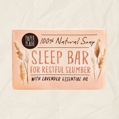 A rectangular bar of Paper Plane Sleep Bar soap in a soft peach-pink color, featuring brown watercolor pampas grass illustrations and black text on a textured beige background.