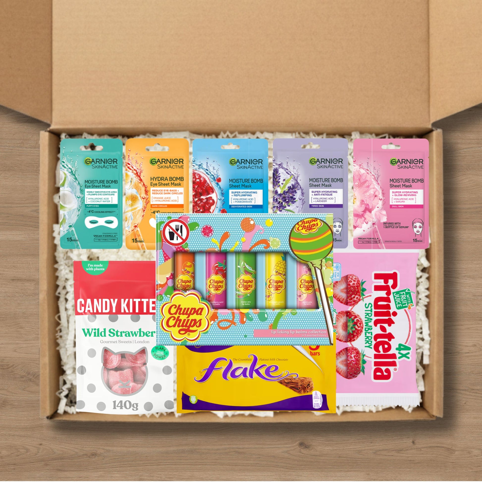 Gift box containing fruit-tella, flake chocolate, chupa chups lip balm, candy kitten sweets, and garnier skinactive face masks