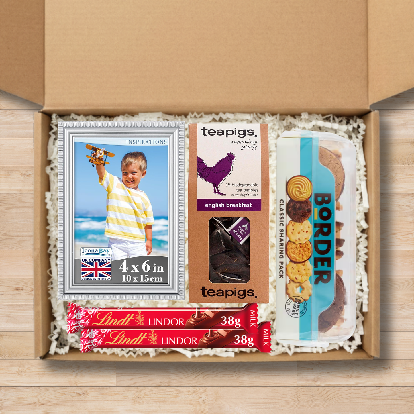 Gift box containing a photo frame, teapigs tea temples, border classic sharing pack of biscuits, and Lindt chocolate bars.