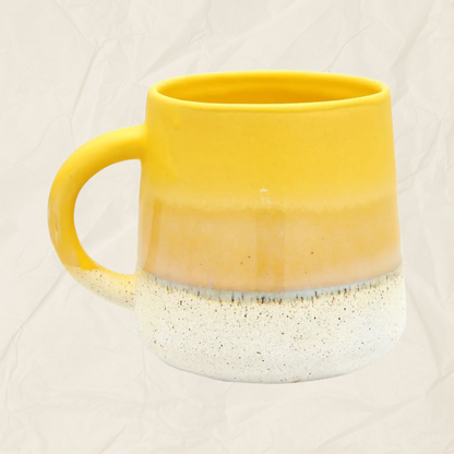 A ceramic mug with a yellow-to-white gradient glaze and a speckled white base, shown against a light beige textured background.